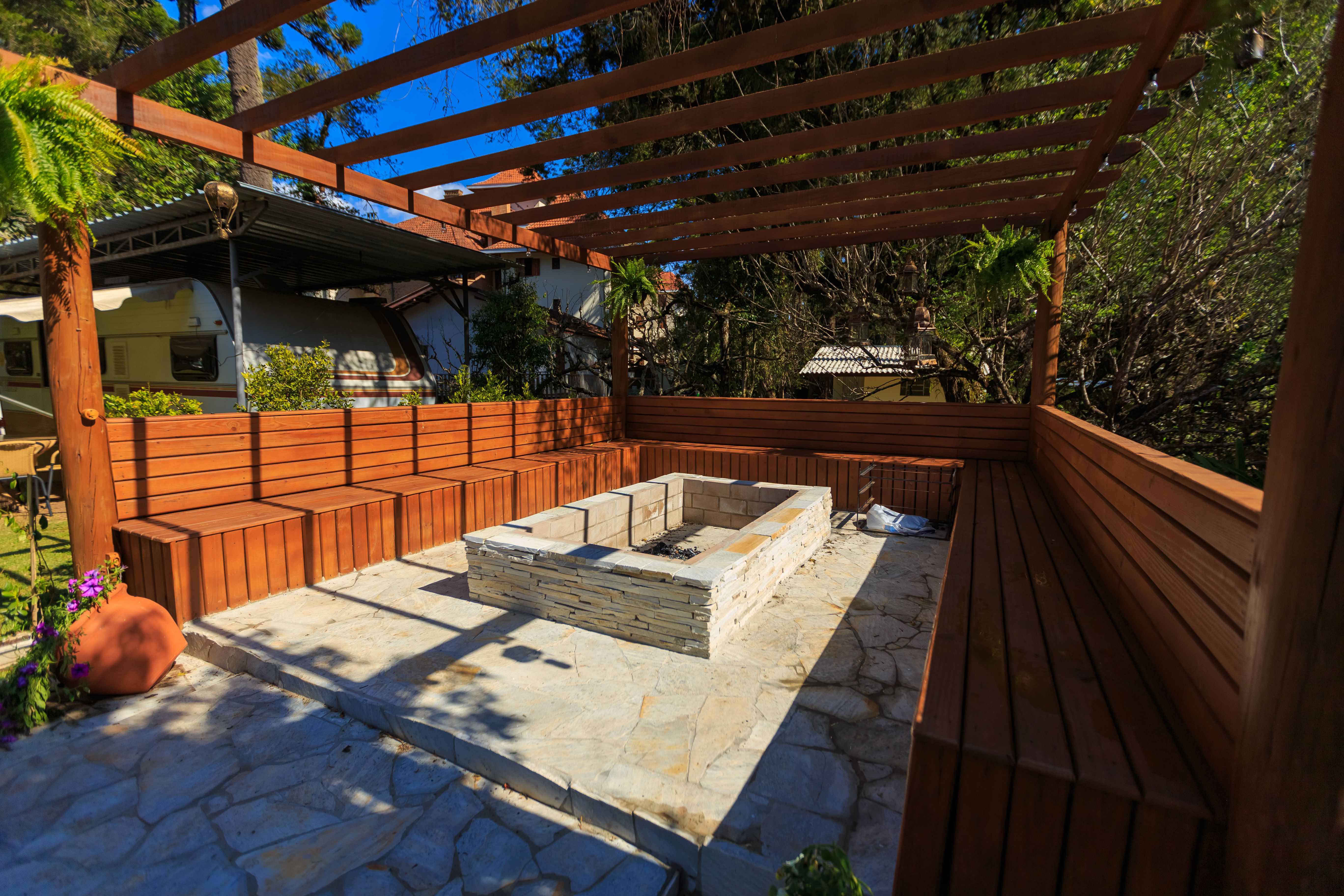 Stone fire pit patio with wooden benches sheltered under a durable pergola