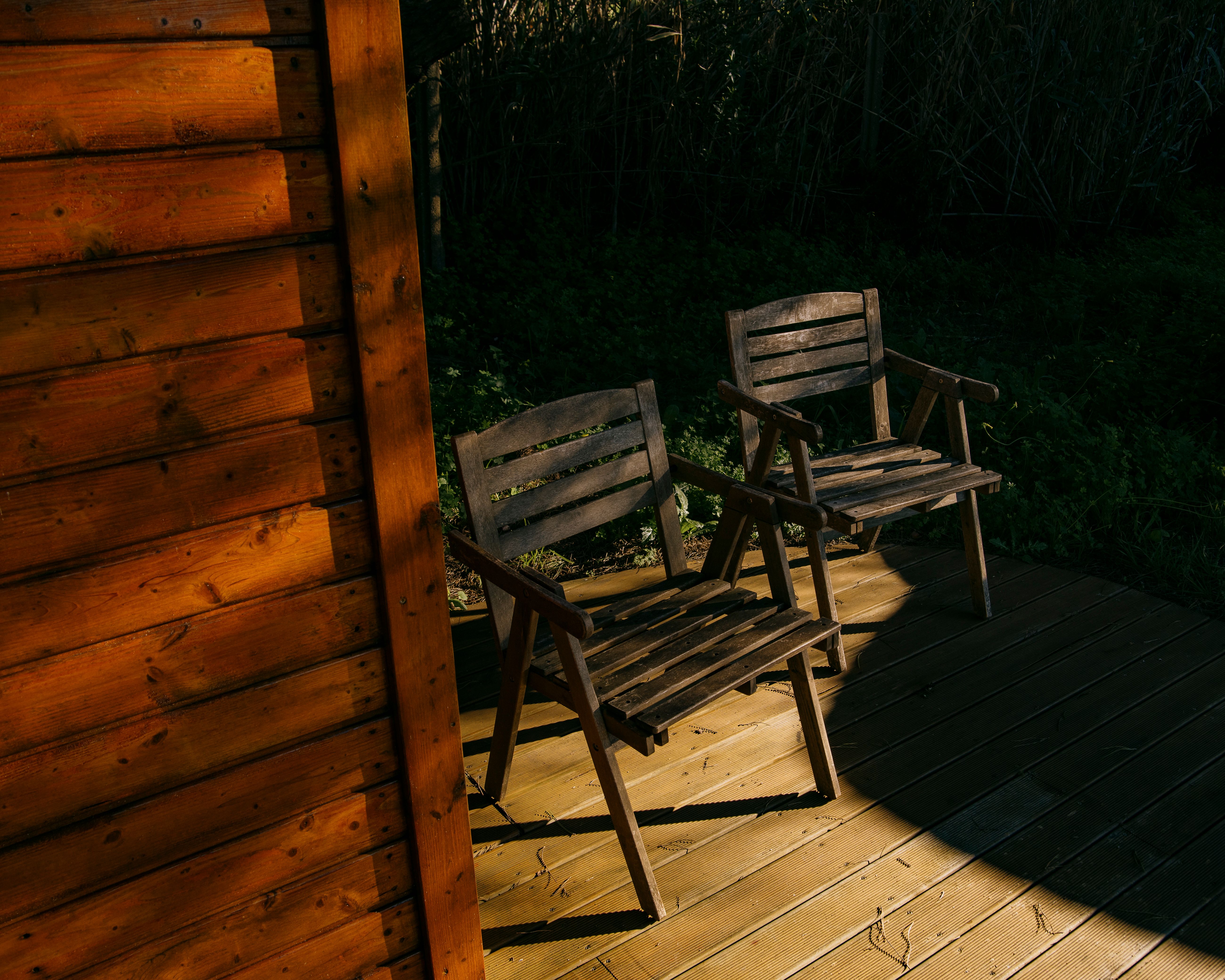 Sturdy wooden chairs arranged on a sunlit deck beside a mountain cabin